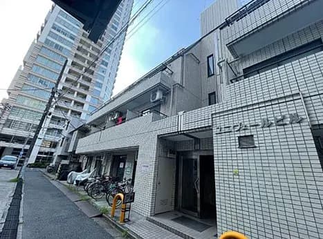 - 都心に立つマンションとその周辺、白いタイルの外観と自転車が置かれた歩道の風景