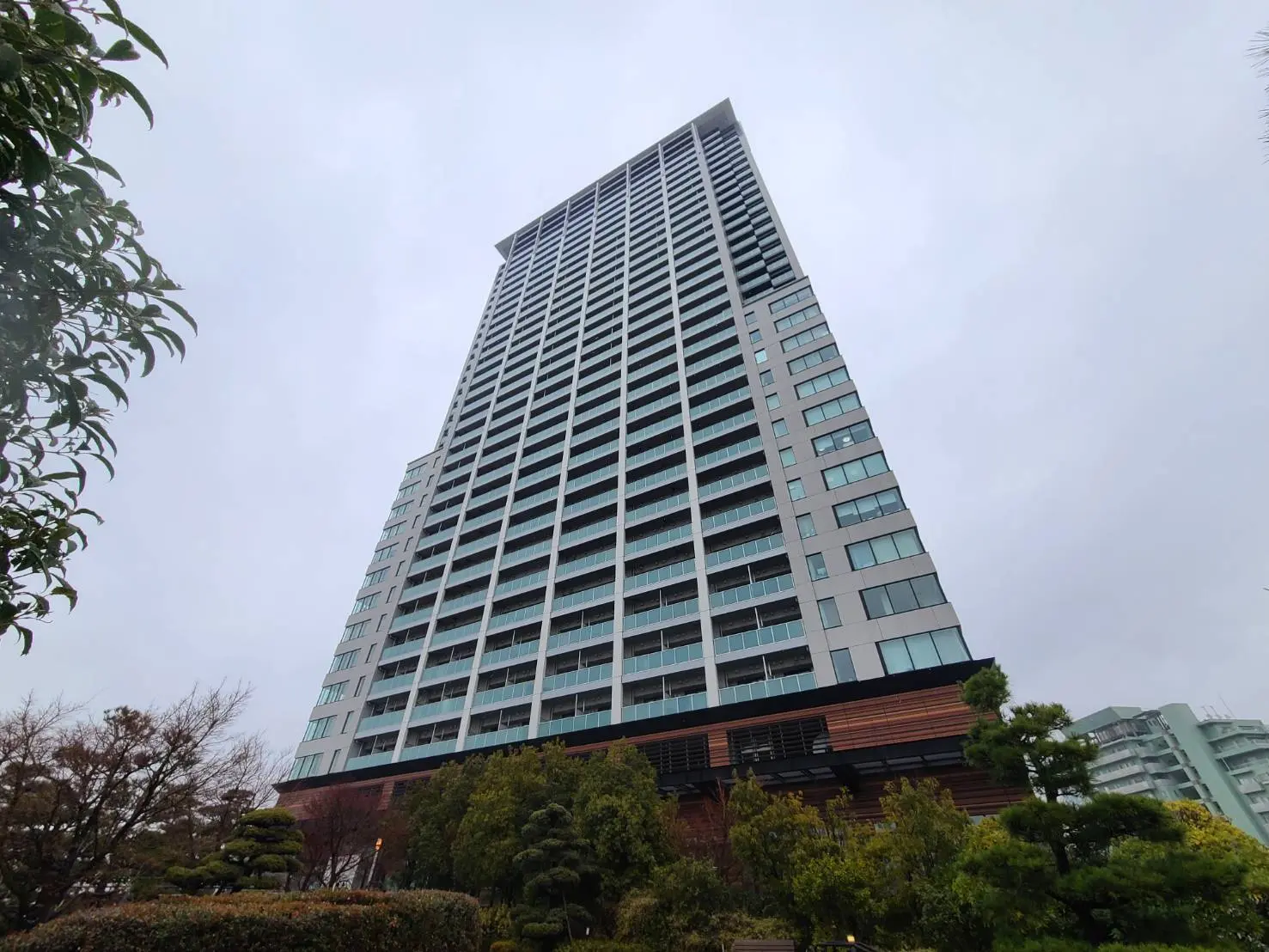 高層マンションの外観、ガラスとコンクリートで構成されたモダンな建築デザイン、緑豊かな公園の前に立つ