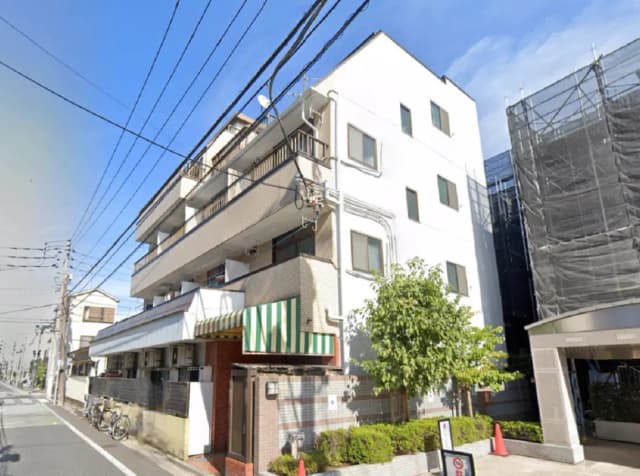 - 日当たりの良い白い外壁のマンション、クリーンなデザイン、周囲に自転車や緑の木々が見える街並み