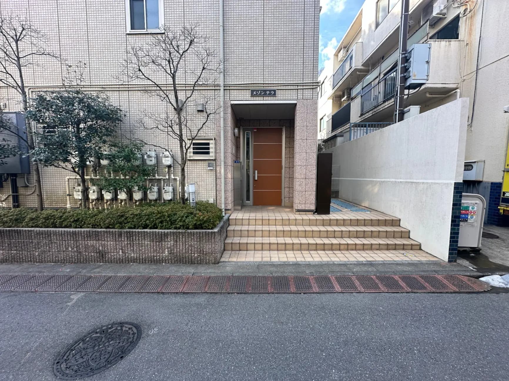 都市風景のアパートメントエントランス、石積みの壁と階段、並木道と道路の舗装