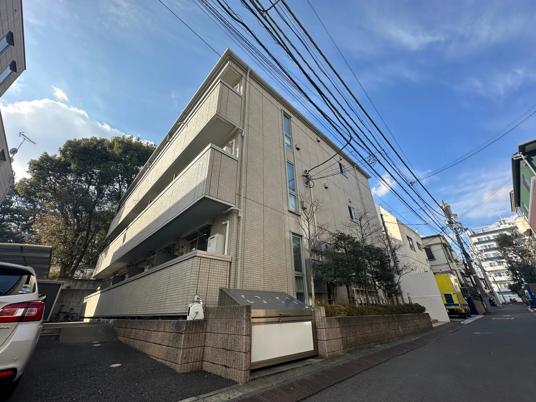 都市の住宅街にあるモダンな外観のアパートビル、青空と電線が交差する景観