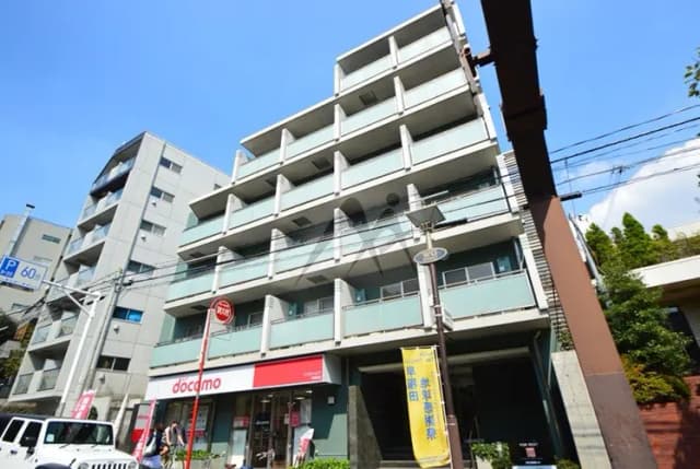 - 近代的な外観のマンション、1階に携帯電話ショップがあり、青空が広がる背景