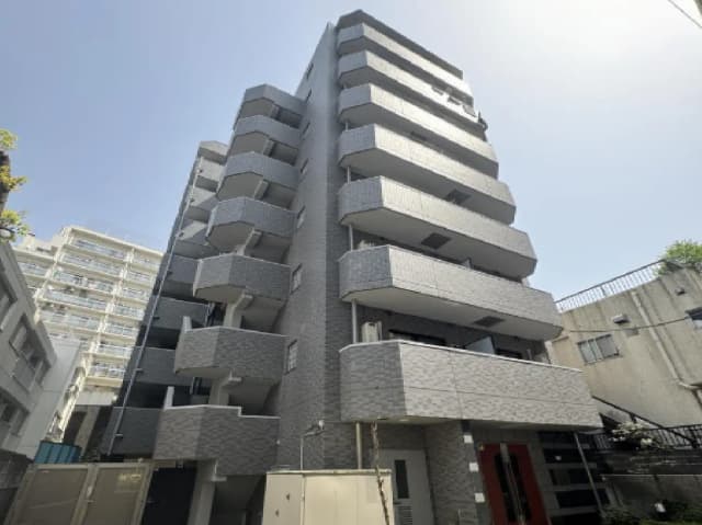 - モダンな外観のオフィスビル、グレーのタイル張り、バルコニーが特徴的で、青空を背景にした印象的なデザイン