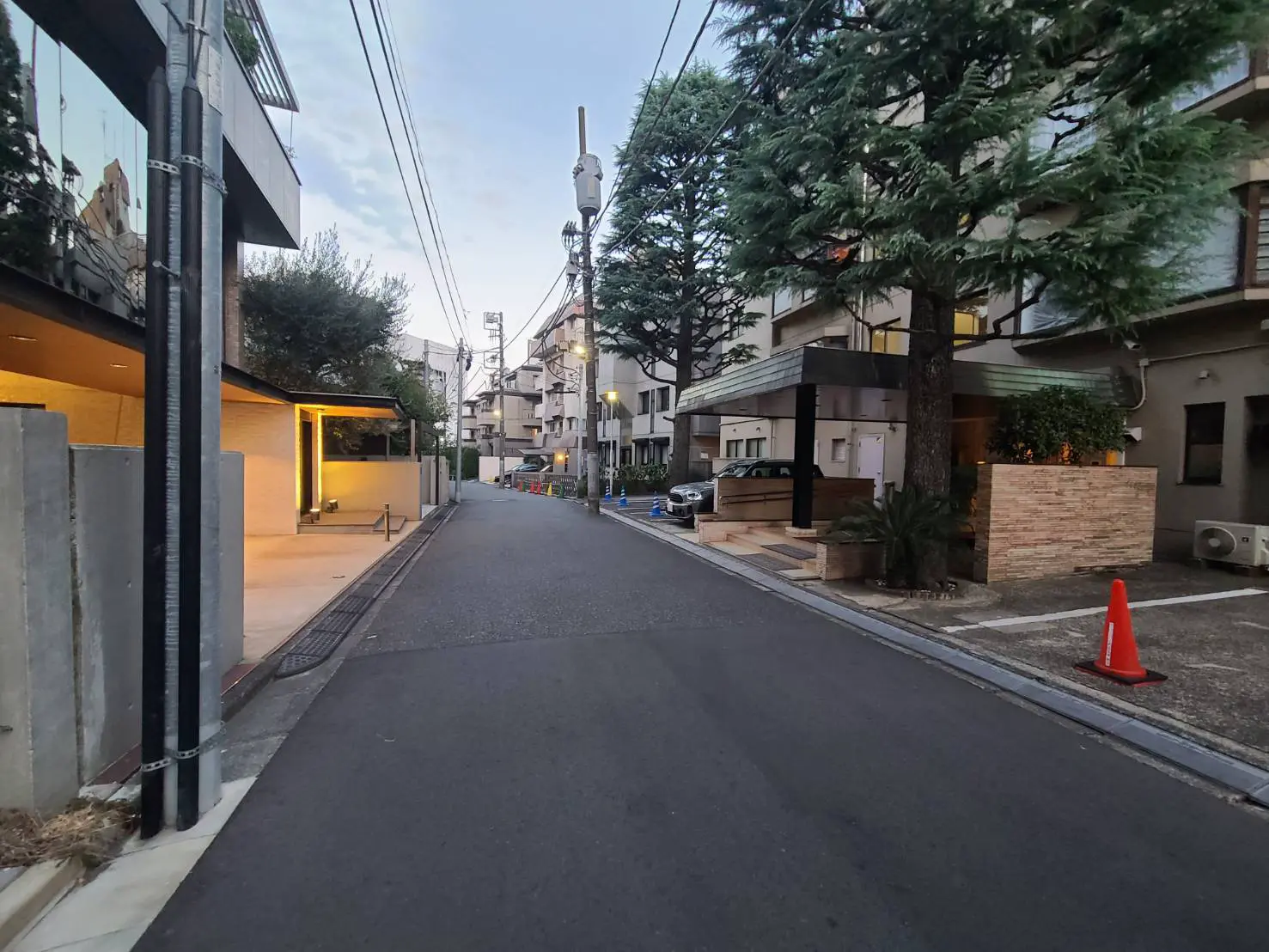 - 都市の静かな通り、両側に並ぶマンションと緑豊かな木々、夕暮れの空が広がる風景