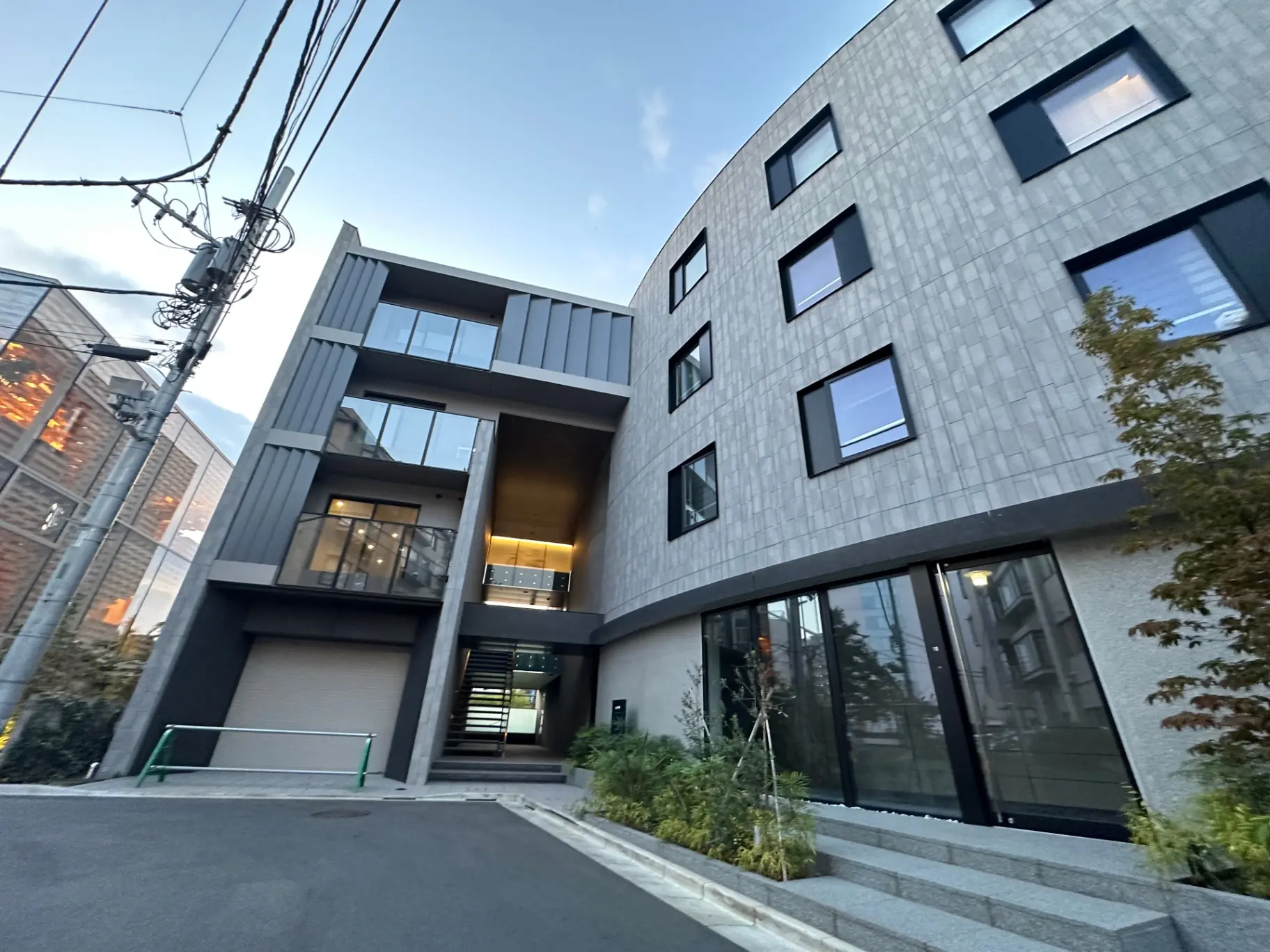 現代的な外観のマンション、グレーの壁に黒い窓枠、街路樹と駐車スペースがある外観デザイン