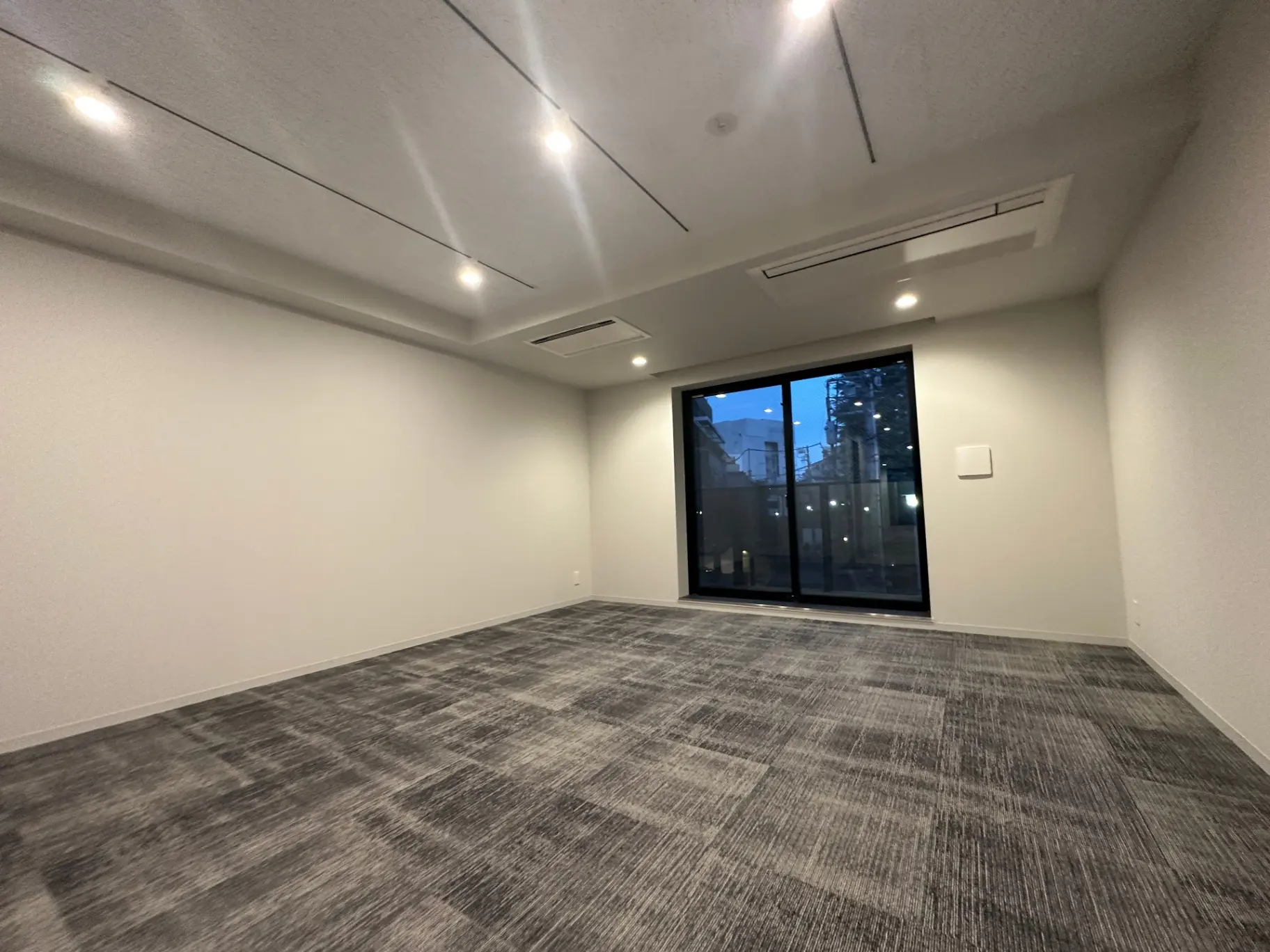 新築マンションの広々としたリビング、ダークグレーのカーペット、大きな掃き出し窓から見える街の景色