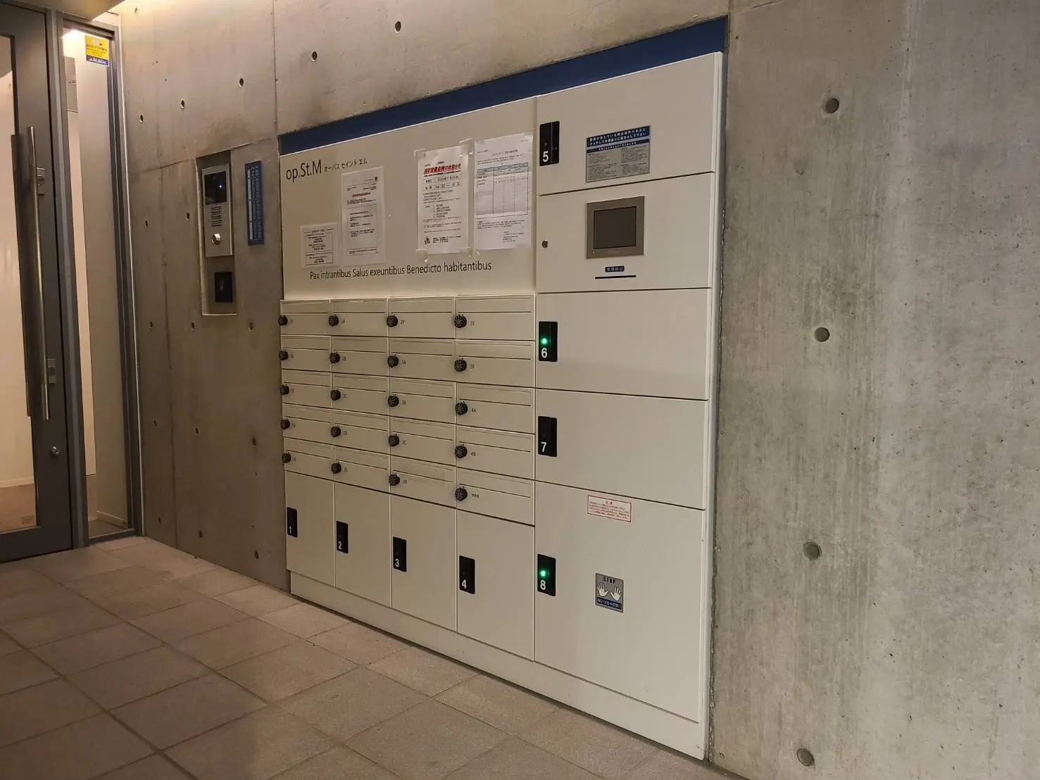 マンションの宅配ボックスとエレベーターホール、コンクリート壁に掲示物、清潔なタイルの床