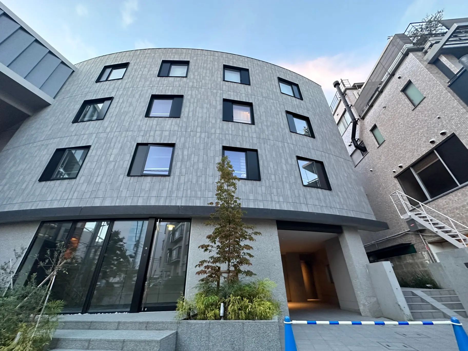 曲線的な外観デザインが特徴的なモダンな建築物、緑の植栽が配置されたエントランス