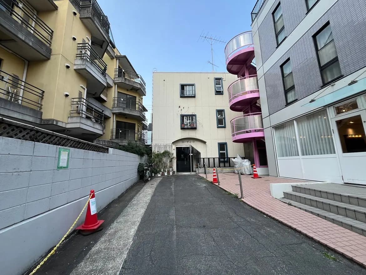 都市の路地にある現代的な建物と螺旋階段、グレーの舗道と赤い交通コーンが見える風景
