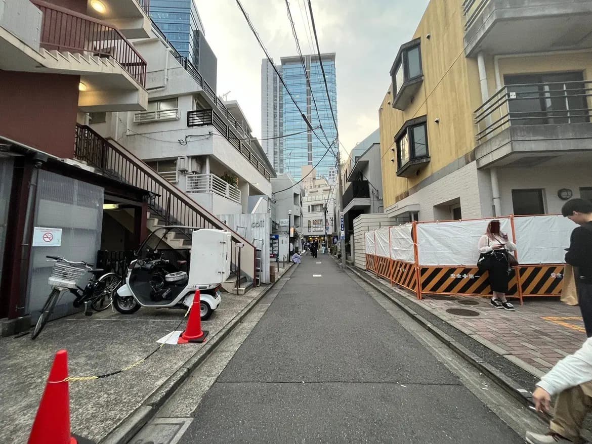 日本の都市の狭い路地、ビルと小さな商店、歩行者とバイクが見える風景