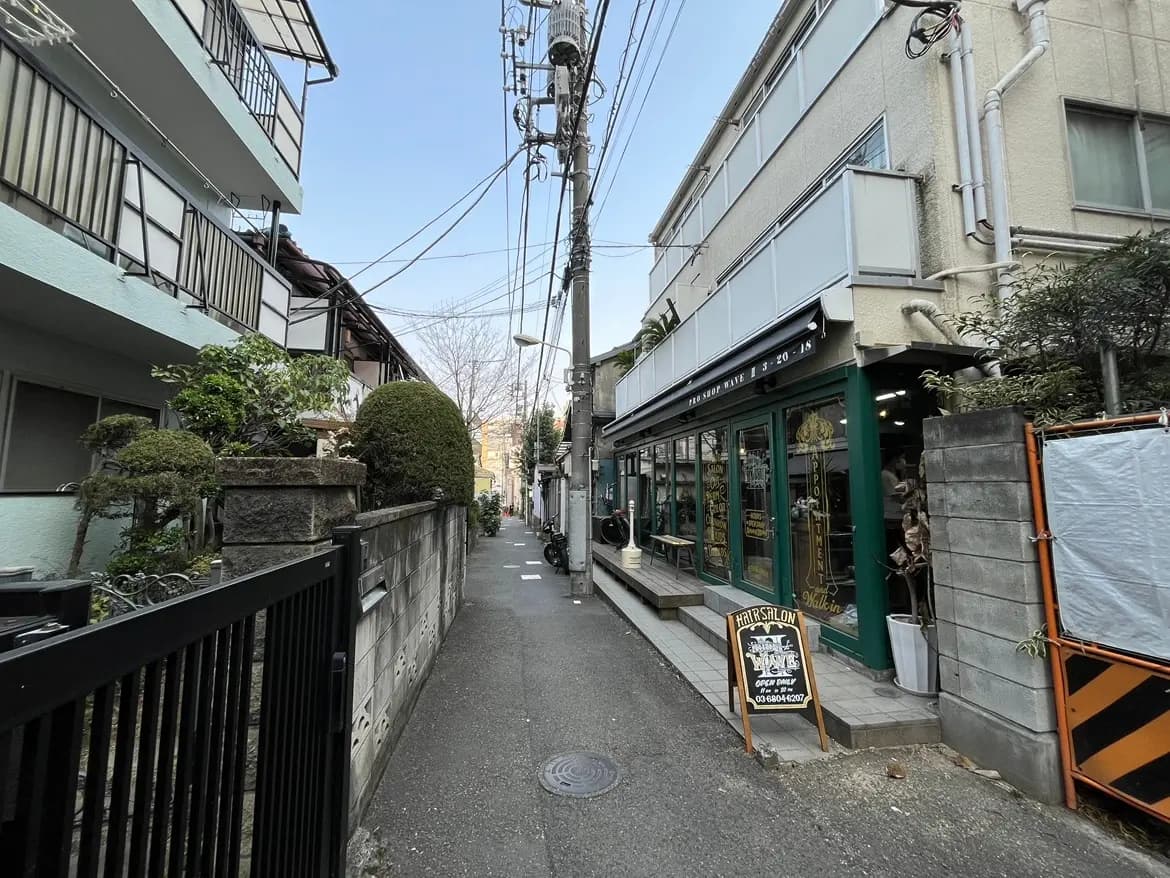 狭い路地に面したおしゃれなカフェの外観、レトロ感のある看板と緑の植物装飾