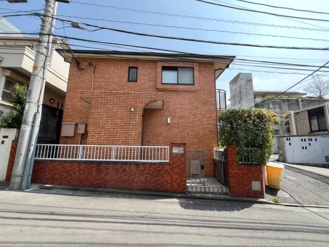 都市の閑静な住宅街にあるレンガ造りの一軒家、前面には植木と白いフェンスが見られる風景