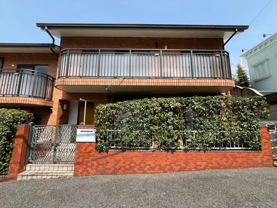 レンガ造りの外壁と植栽に囲まれたモダンな一戸建て住宅、バルコニー付きデザイン