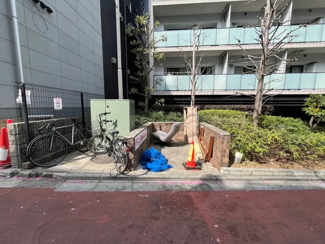 都市のアパートメント横の自転車駐輪場、工事中の看板、背景には樹木と建物