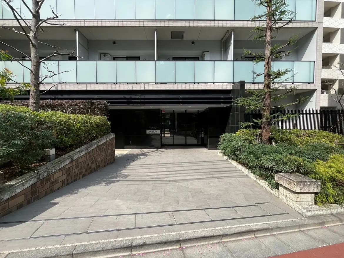 モダンなマンションのエントランス、整備された緑の植栽、クリーンな歩道と明るい日差し