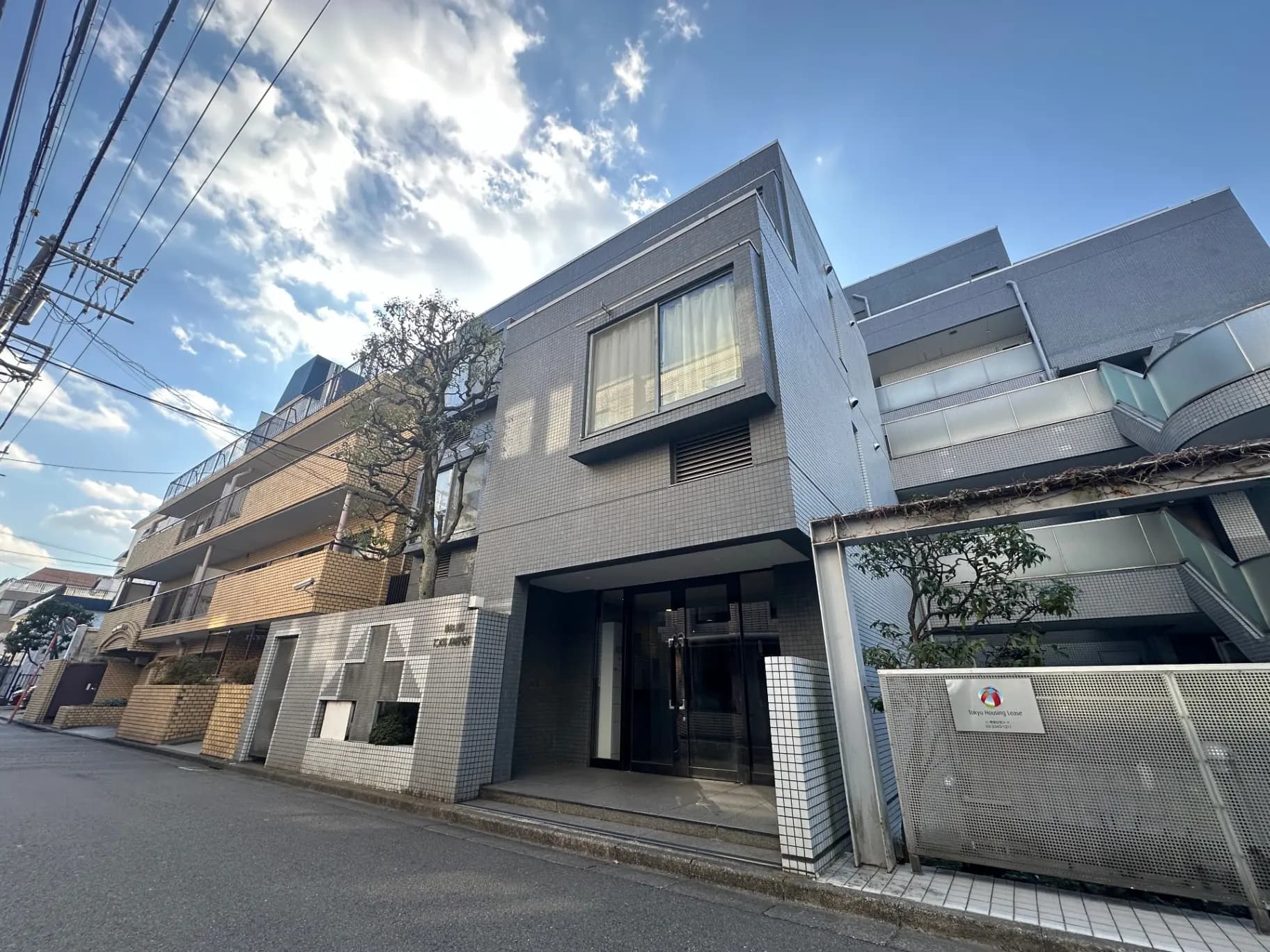 現代的なデザインの都会的な外観、グレーの壁と大きな窓、青空と白い雲が広がるクリアな日中の風景