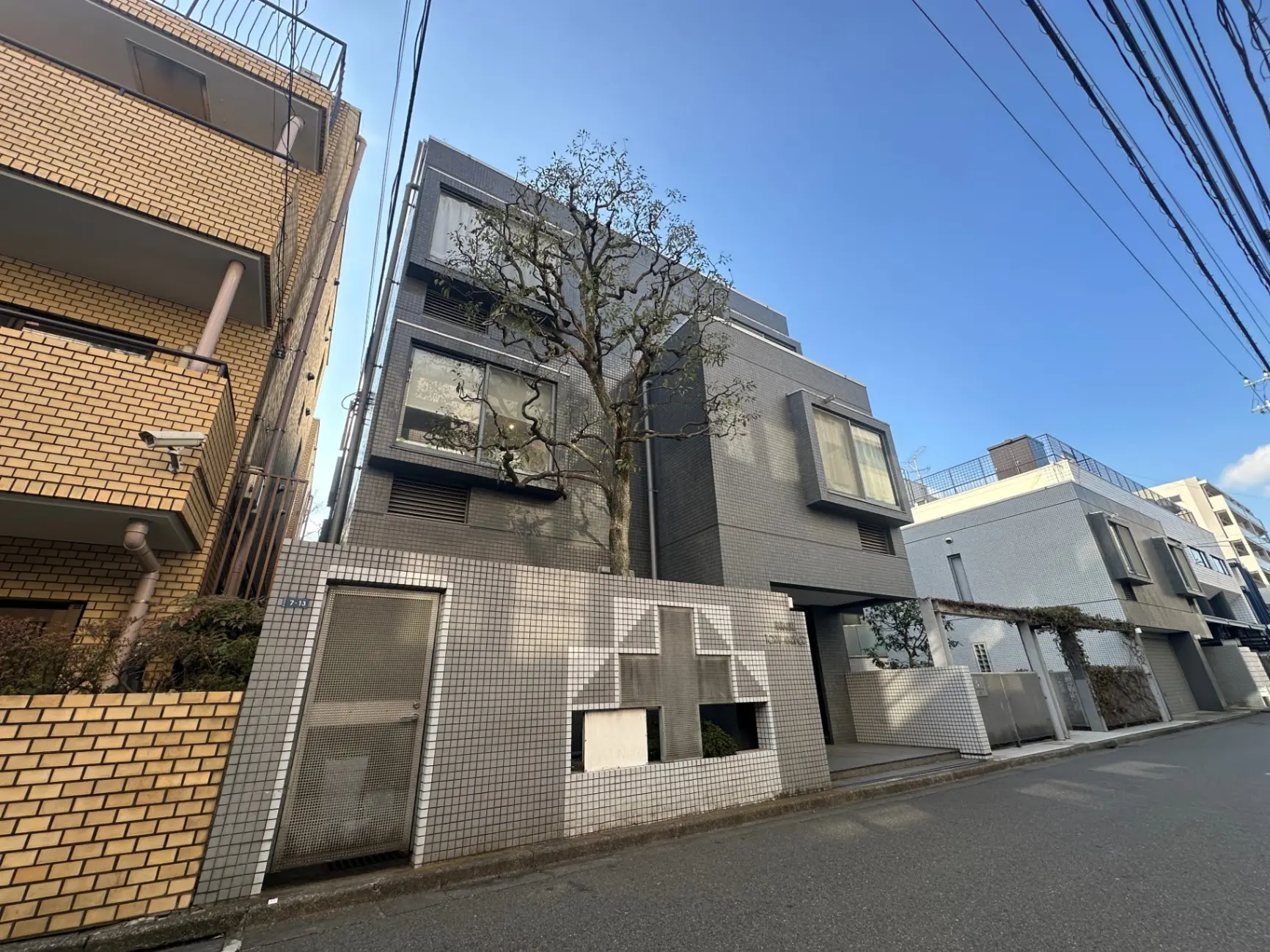 現代的なデザインの都市型住宅、黄色とグレーの外壁、街路樹が並ぶ通り