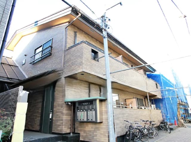 - レンガ調の外壁を持つ二階建ての住宅、入口付近に郵便受けと自転車置き場がある外観