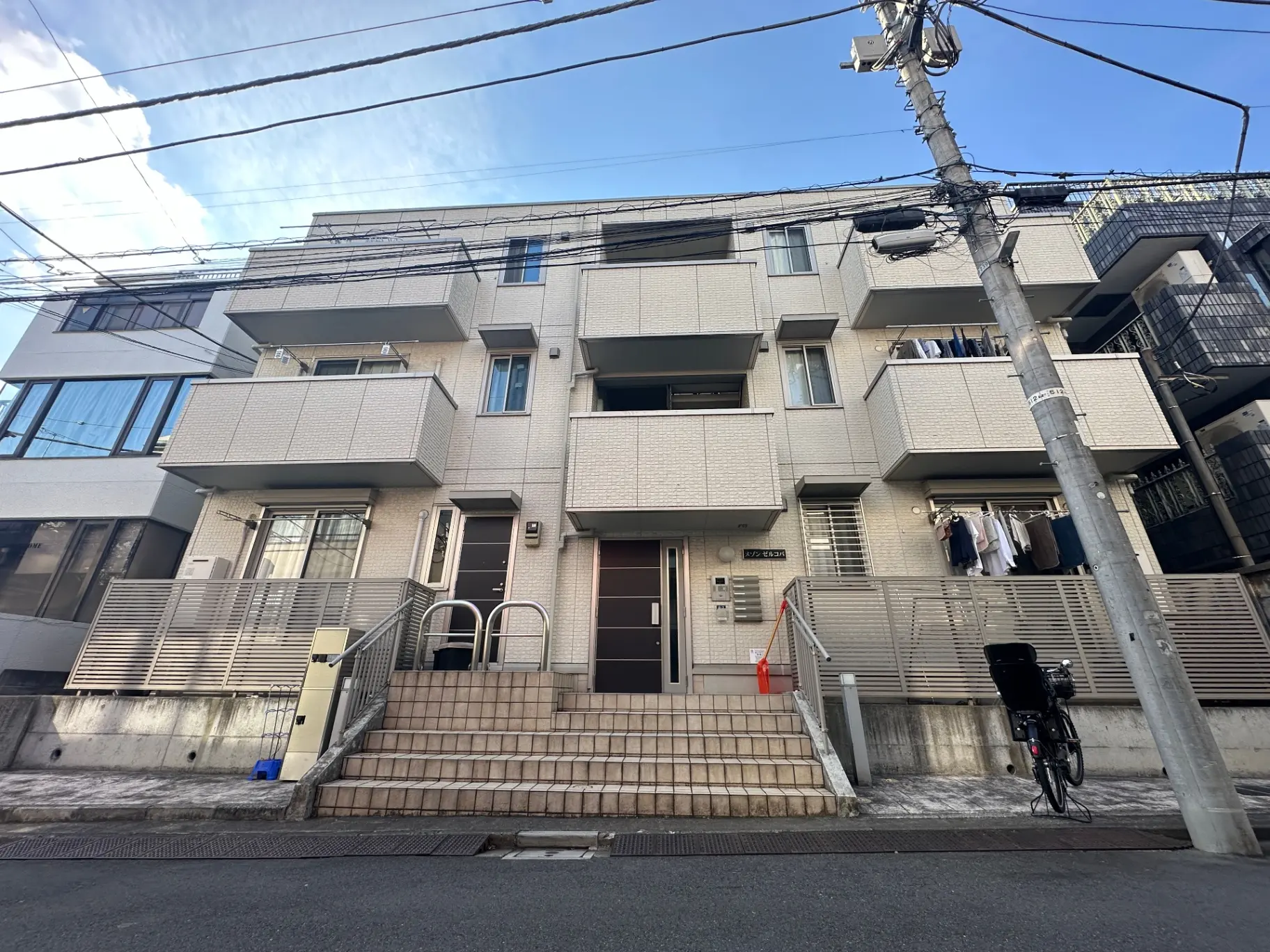 日本の郊外のモダンなアパートの外観、白い壁に囲まれたバルコニー付き、洗濯物が干されている