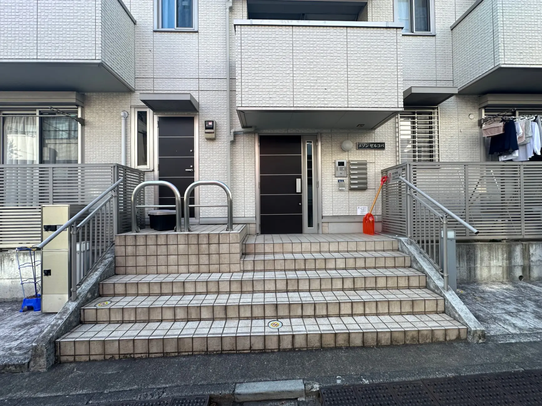 都市型のアパートの玄関、石畳の階段とスチールの手すり、郵便受けと洗濯物が干されているバルコニー