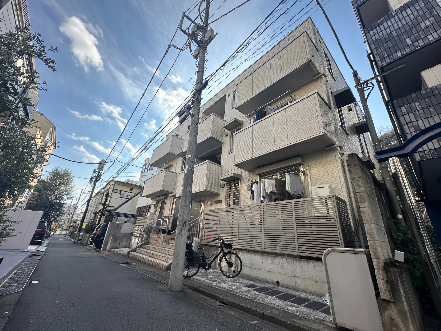 日本の住宅街、電柱と配線が並ぶ狭い道路、ベランダで洗濯物が干されているアパートメント