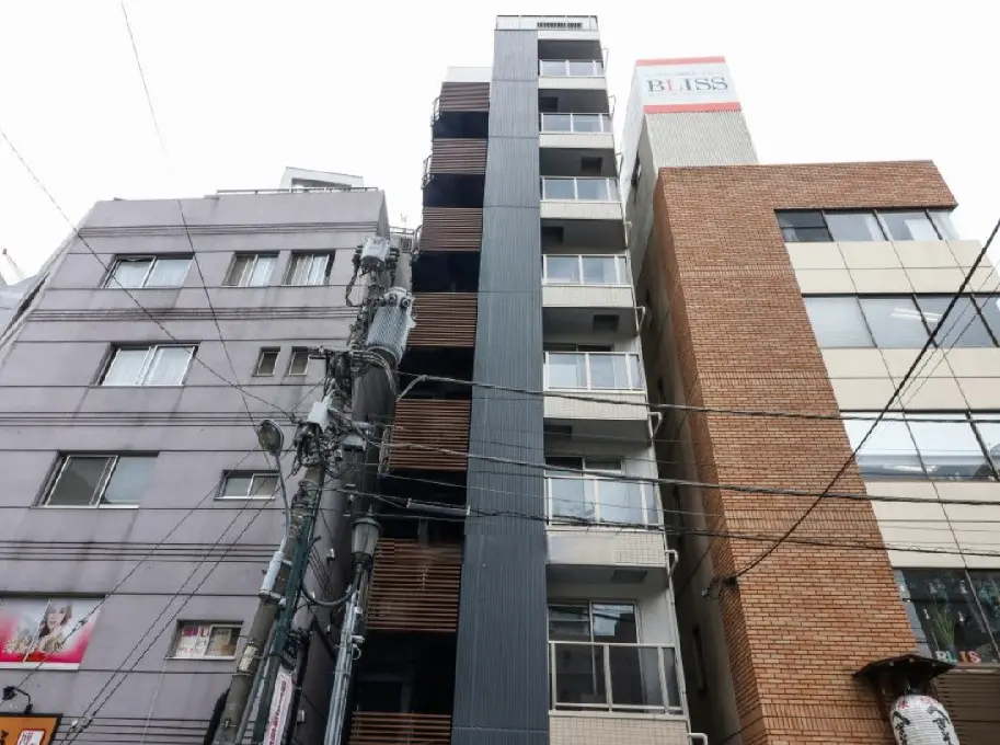 - 都市的なデザインのビル群、グレーの外観と木製バルコニーが特徴の建物、周囲には電柱や電線が交差する風景