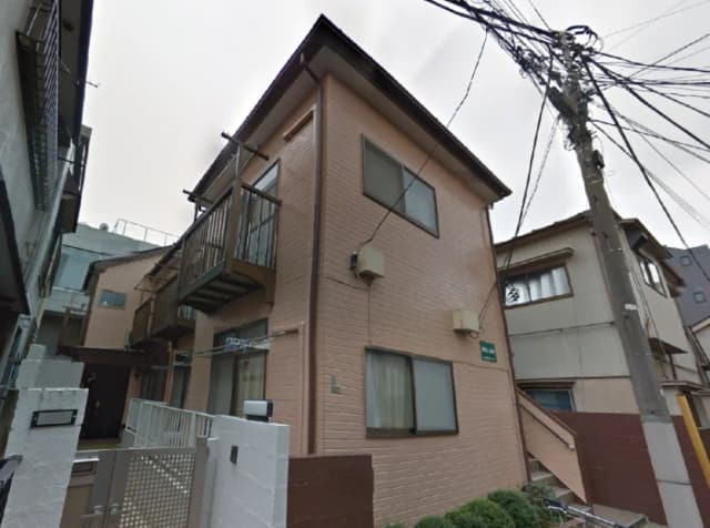 - 外観が淡いピンク色の二階建ての住宅、バルコニーと窓があり、周囲に電線が多く見える構造