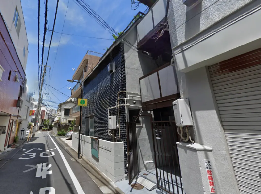 - 都市の住宅街にある黒タイルの外壁が特徴のビル、近くには電柱と道路標識が見える風景
