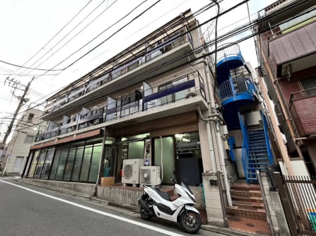 - 白いスカウトバイクとガラス張りの店舗入り口がある、近代的なアパートメントビルの外観、青い階段と電線が交差する風景