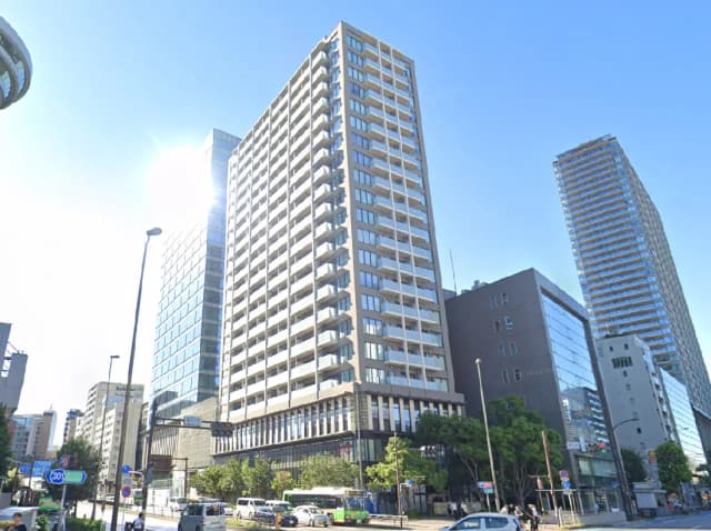 - 都市景観を背景にした高層ビル群、中央にはモダンなデザインの建物がそびえ立ち、青空の下で明るい印象を与える風景