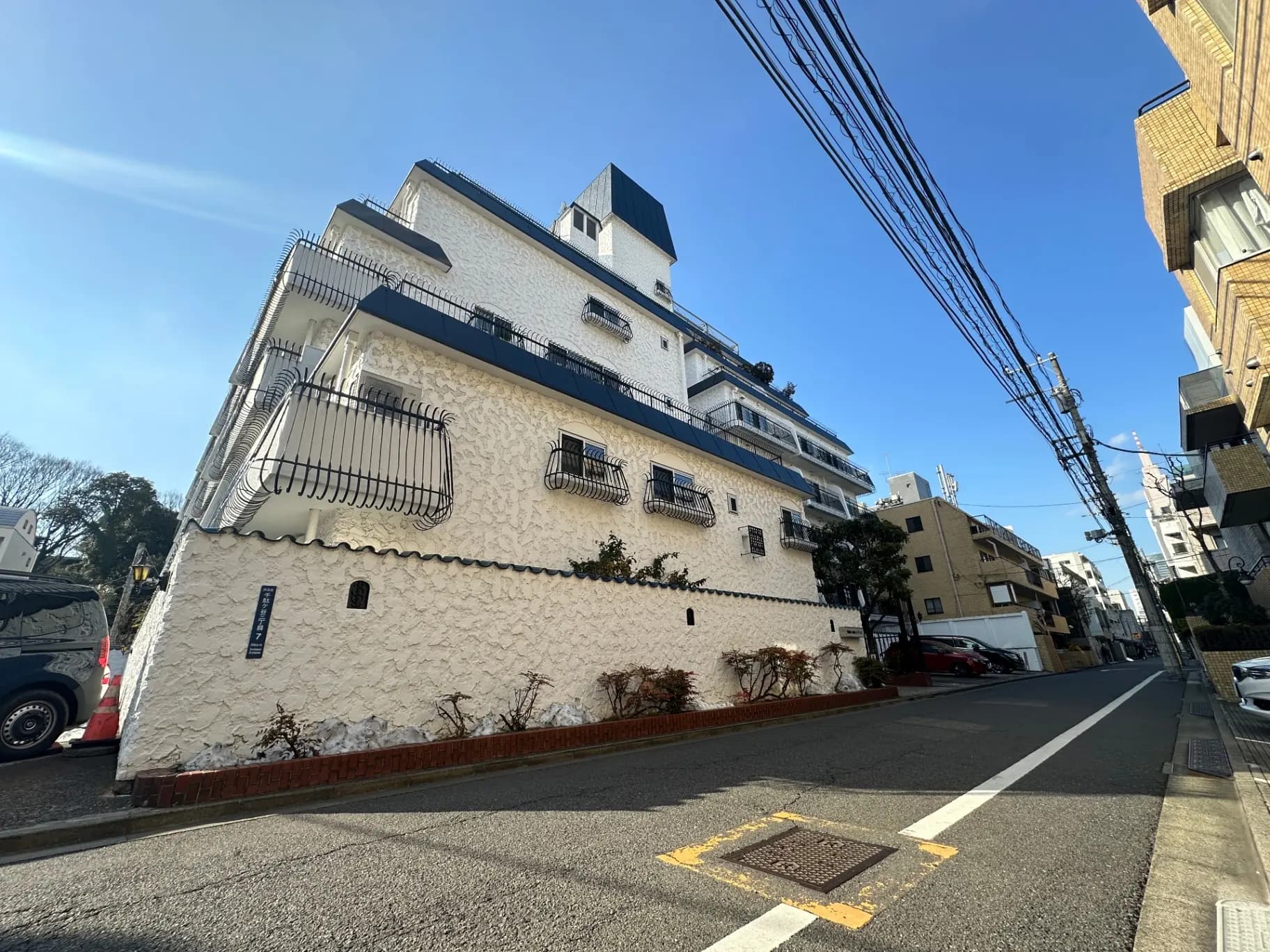 都会の住宅街に立つヨーロピアンスタイルのアパートメント、白い外壁と青いバルコニーが特徴