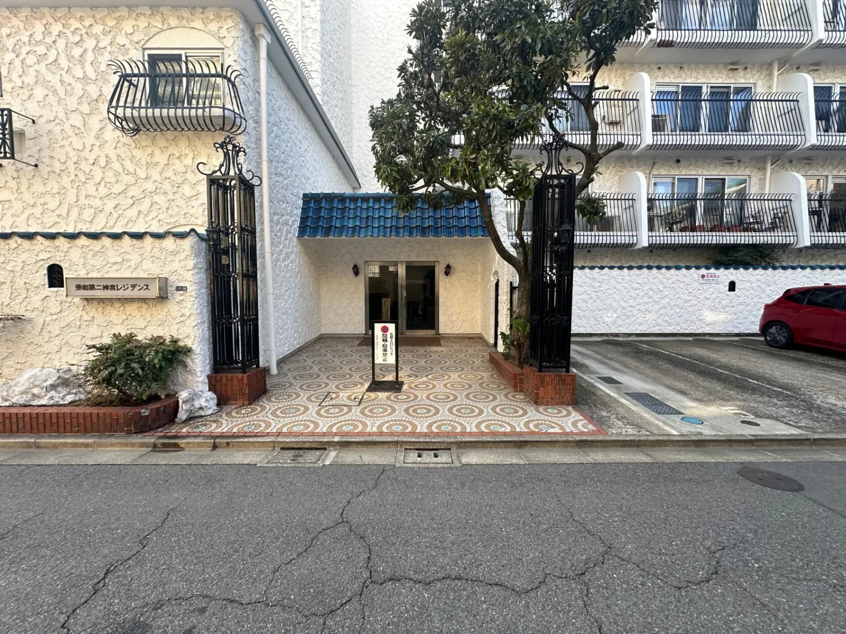 ヨーロピアンスタイルのアパートメント外観、白い壁に青い屋根、エントランスには鉄製の装飾ゲート