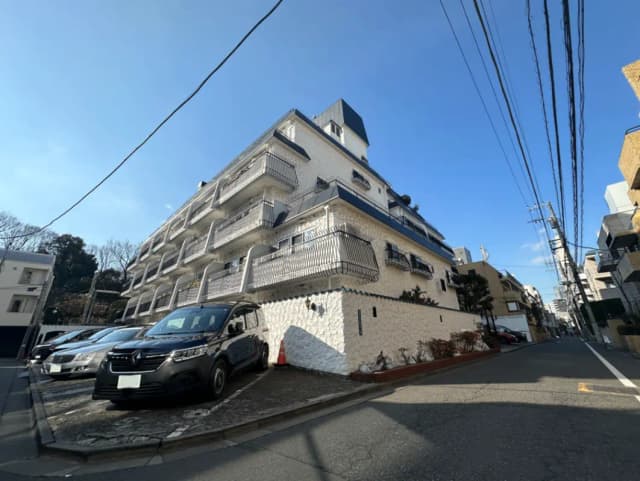 日差しの中にあるホワイトとブルーの外装のマンション、バルコニー付きの多階建て住宅、駐車場に車が並んでいる都市風景
