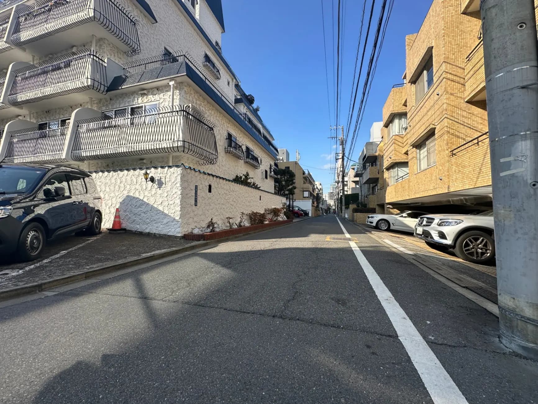 日本の住宅街、路地に面した白い壁のアパートとタイル貼りのマンション、駐車場に停まる車、青空と日差しが映える街並み