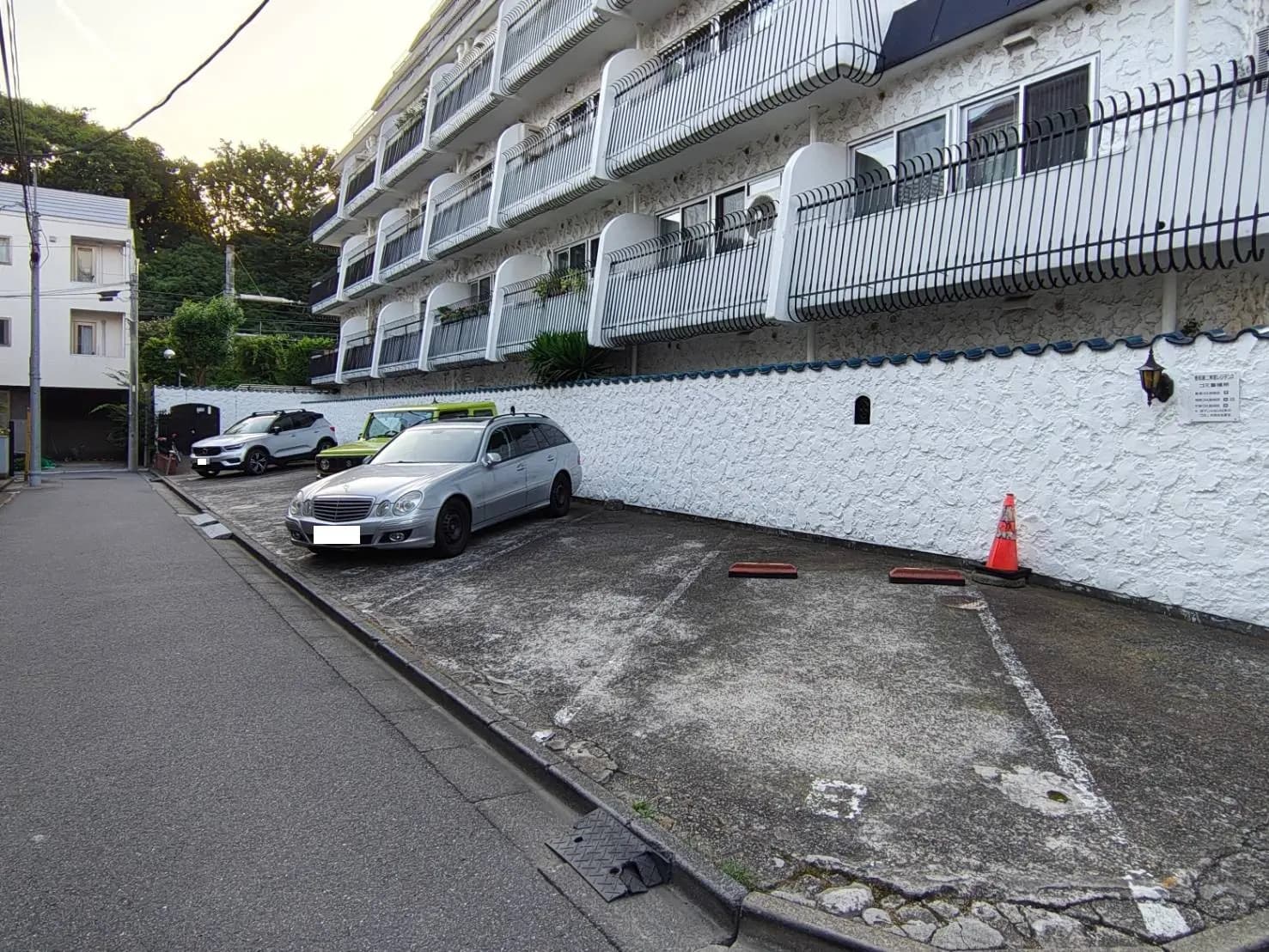 - 駐車場に停まっているシルバーの車と周囲の建物、白い壁と植栽が並ぶ風景