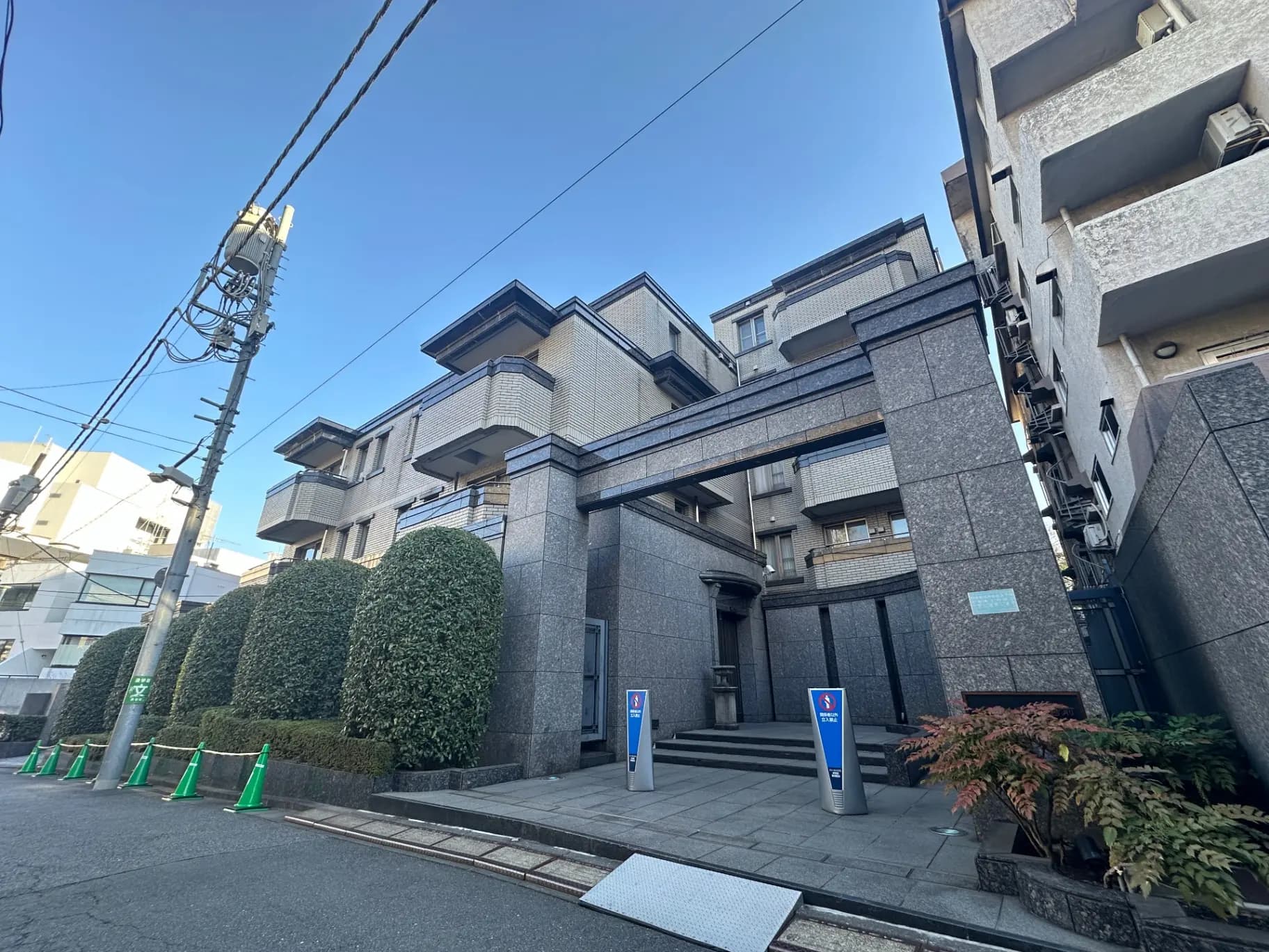 都心の高級マンションエントランス、石造りの壁、植栽の緑と快適な住環境