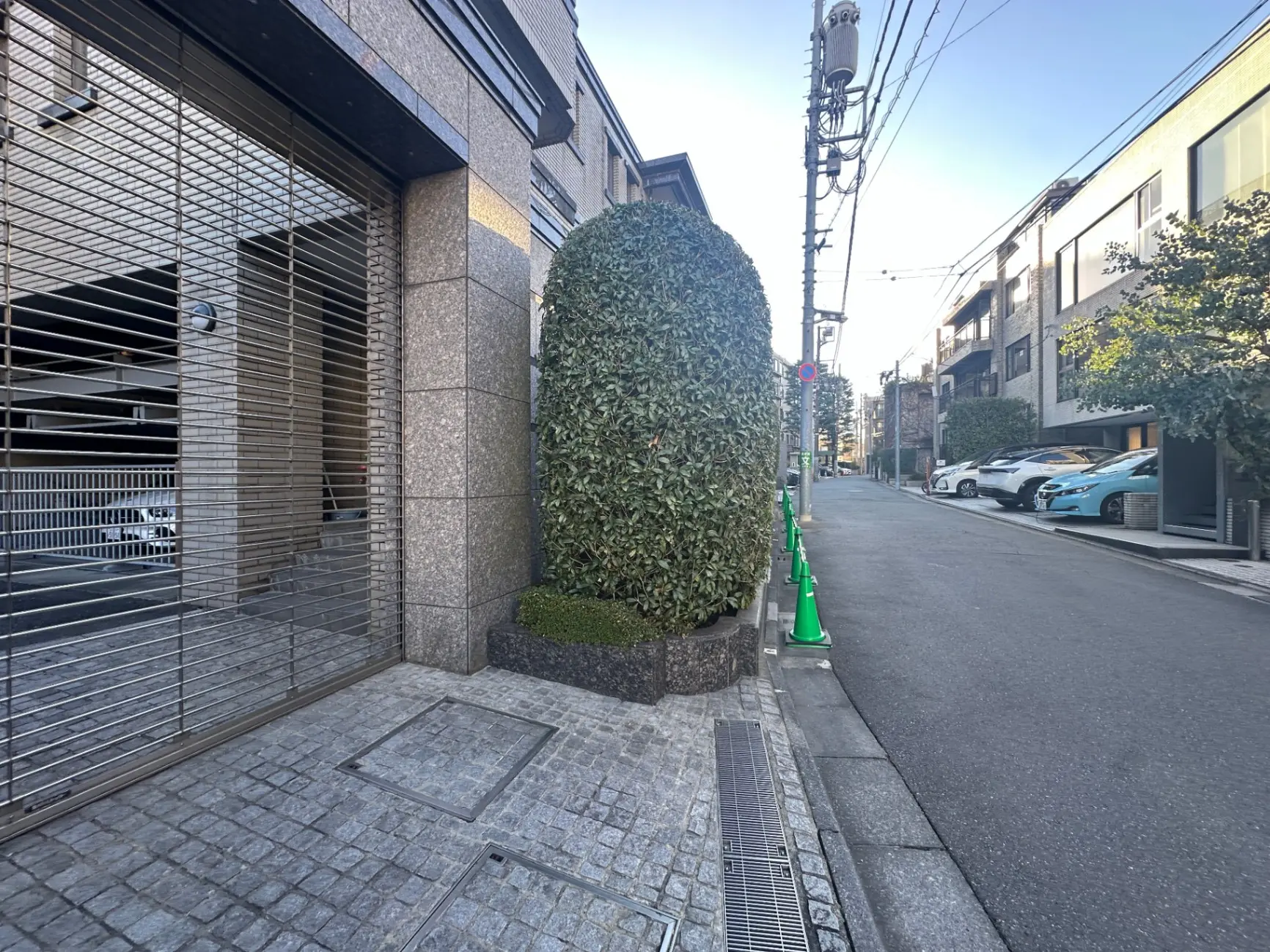 日本の都市の石畳の道路と建物、植木のある歩道、駐車された車のある風景