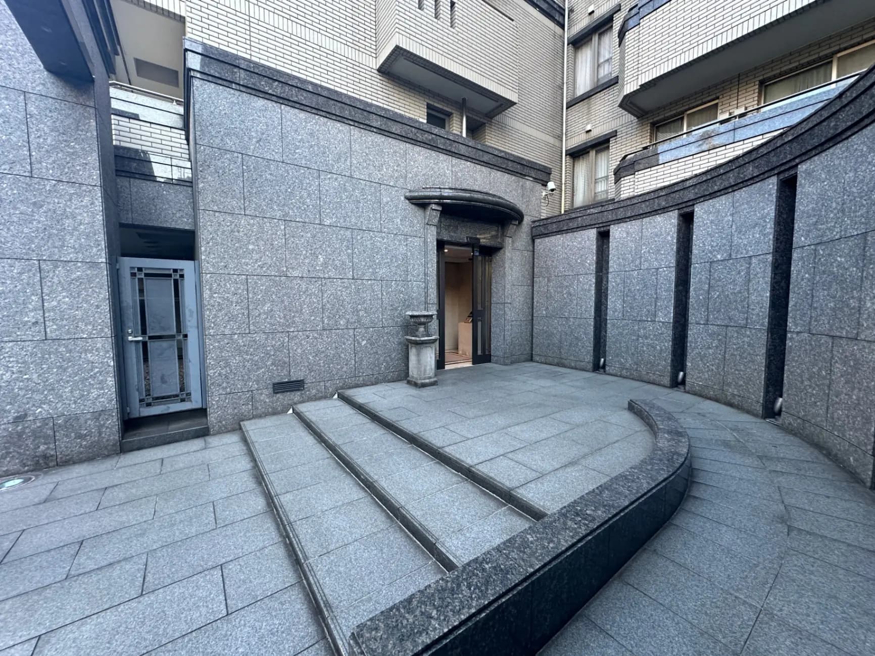 都会のビルの間にある石造りのエントランスと階段、モダンなデザインの外観