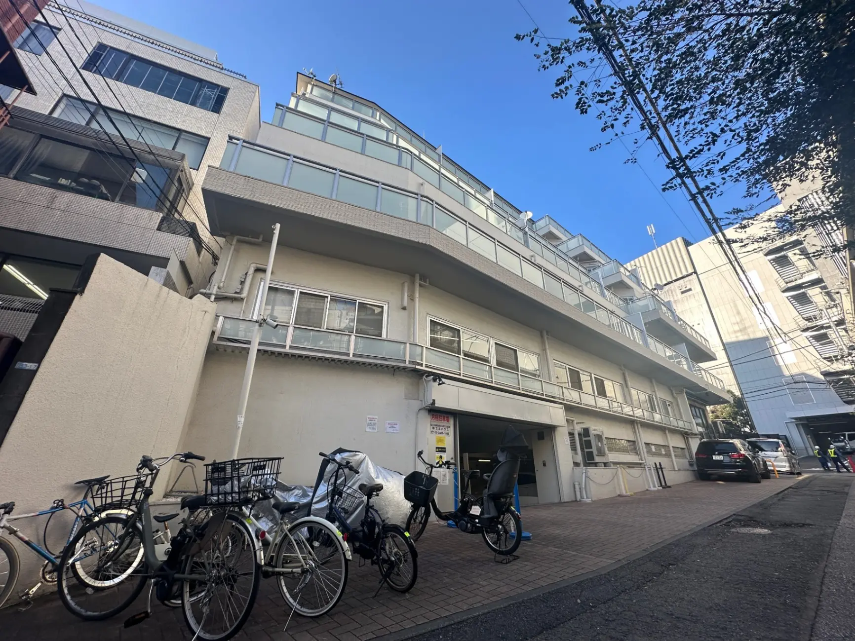 都市部のアパート建物外観、自転車駐車場と駐車スペース、晴れた日の青空