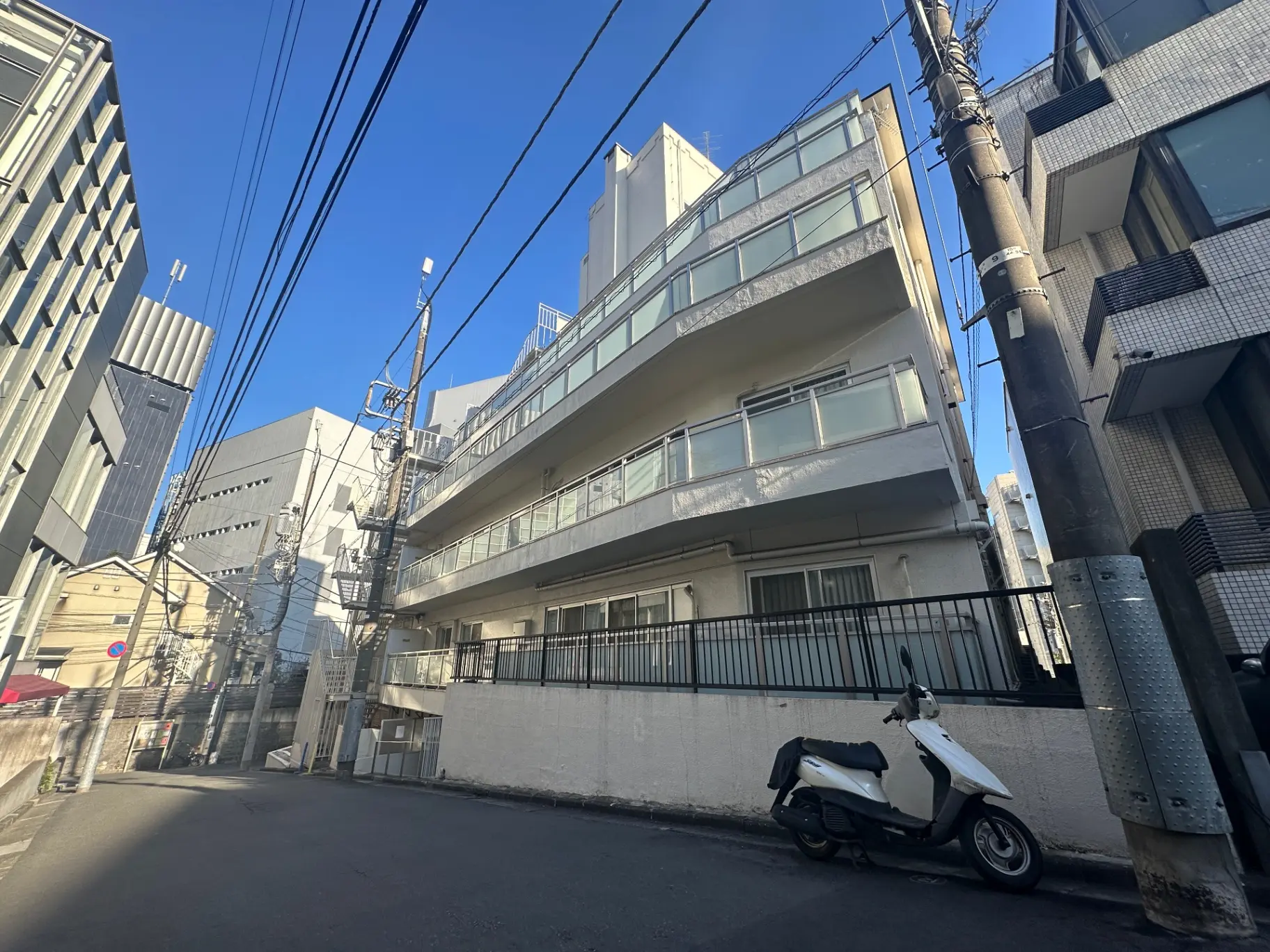 都市の住宅街の路地、青空と近代的なビル、スクーターが駐輪された街並み