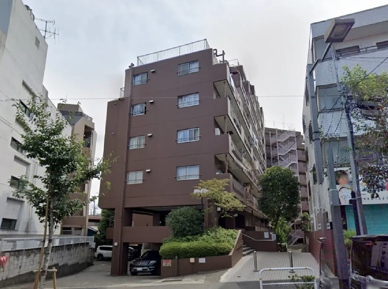 - ブラウンの外壁を持つ住宅ビル、周囲に緑の植栽があり、駐車スペースと階段のあるエントランスが見える景観