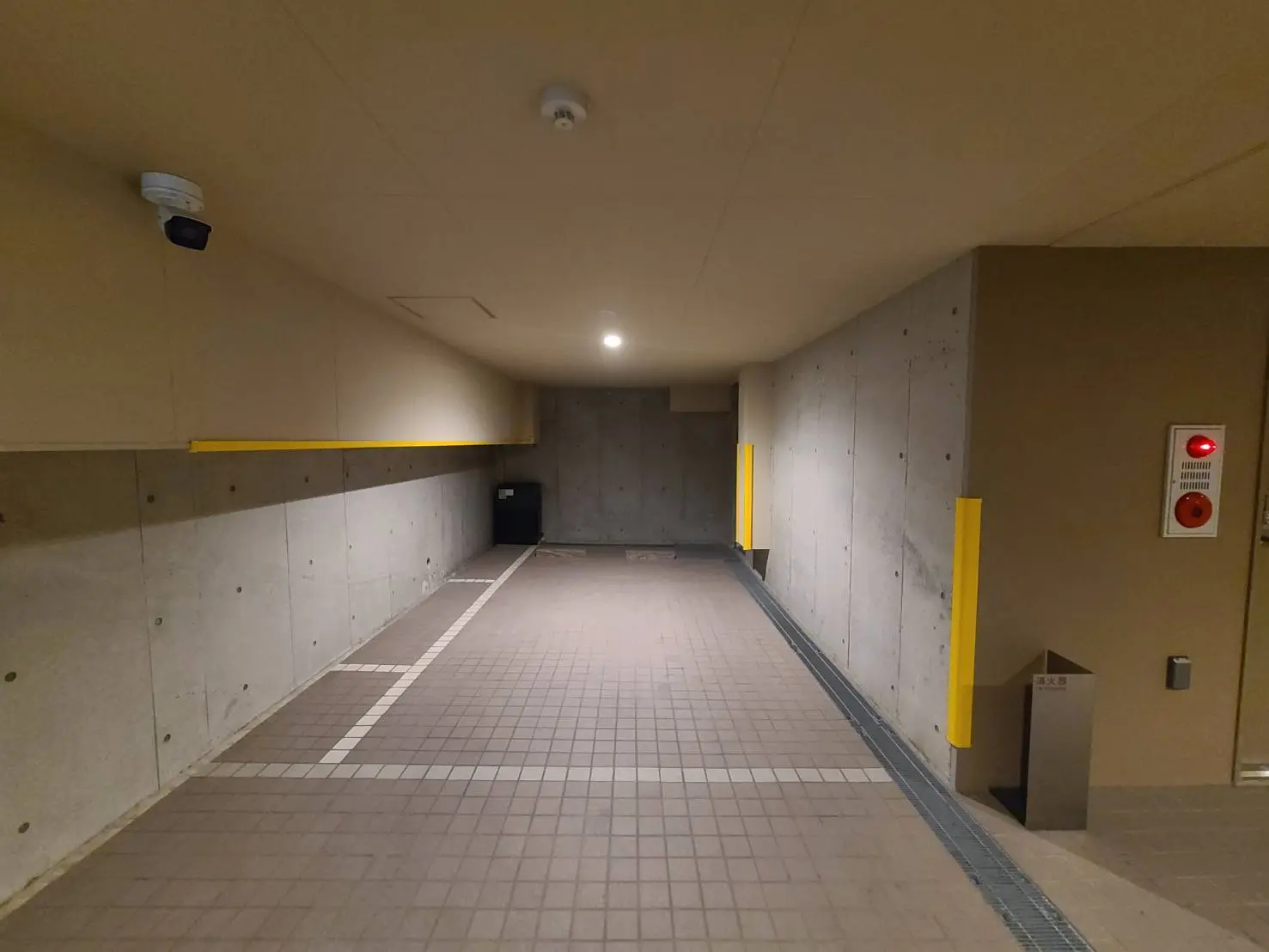 清潔で広々とした地下駐車場の通路、コンクリート壁と床、黄色の安全線、緊急火災警報器が設置されている