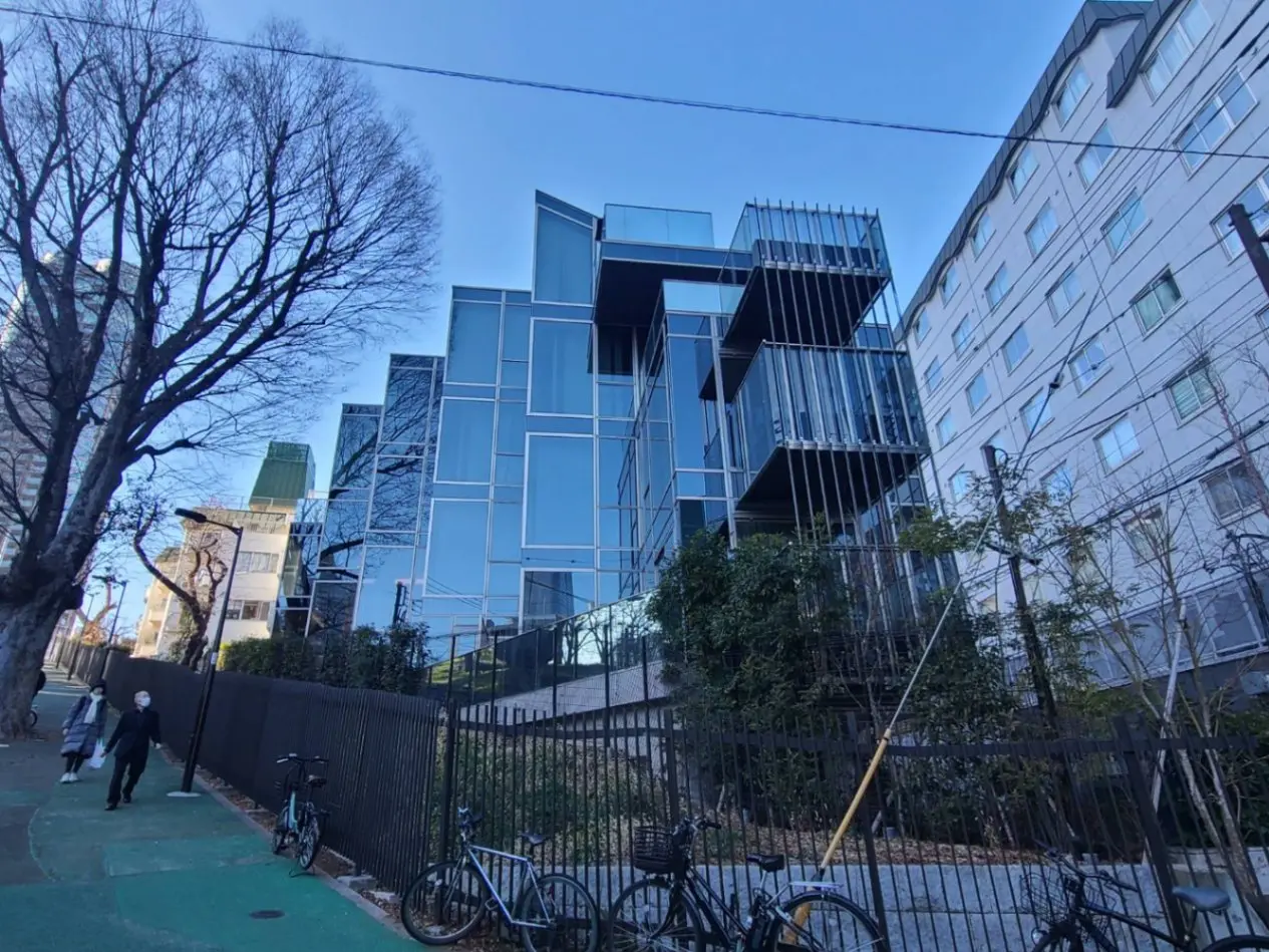 青空の下、ガラス張りのモダンな建築物と街路樹、自転車が停まっている都市風景