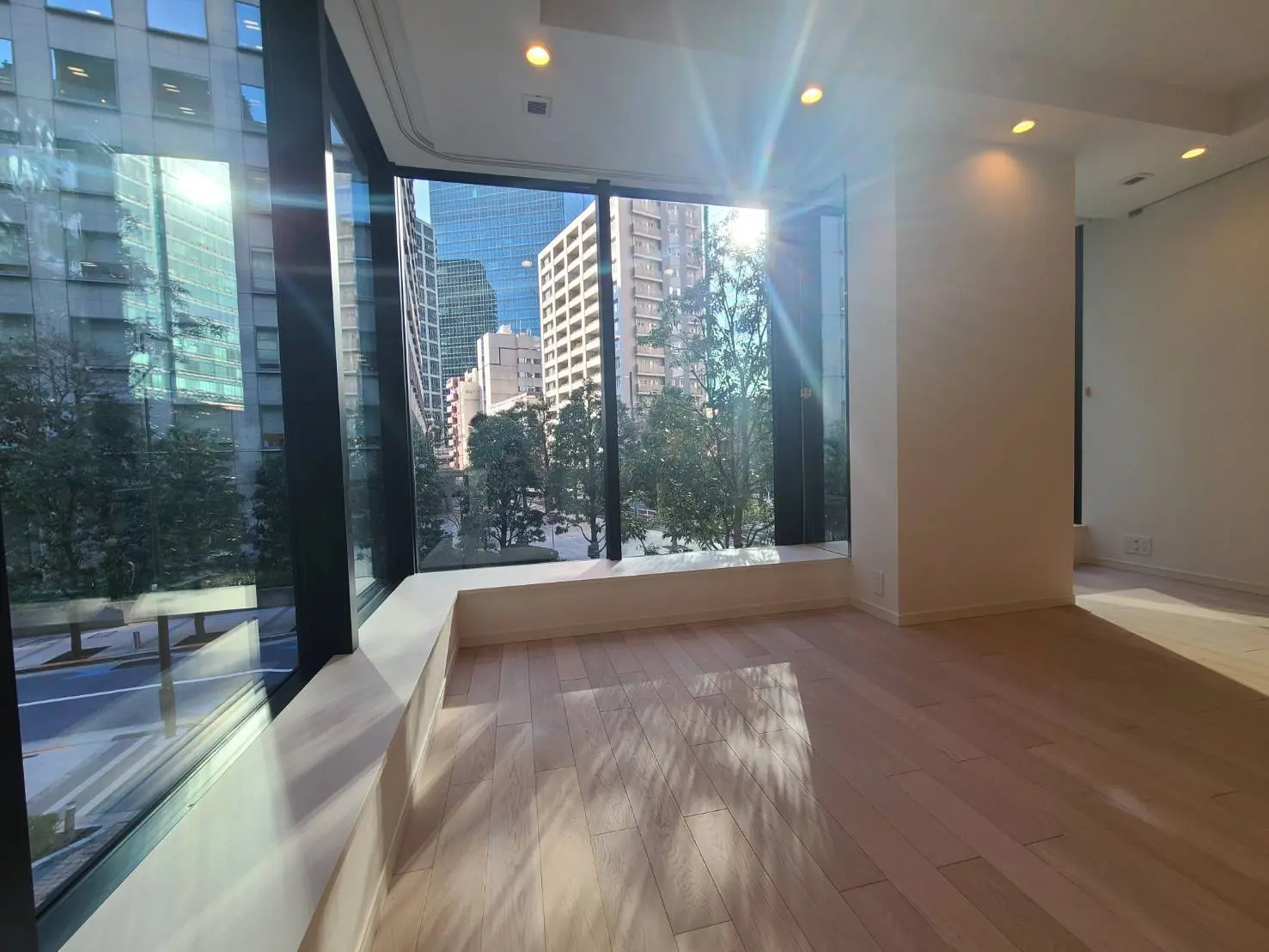 都心に位置する明るく開放的なリビングルーム、大きなガラス窓から見える都会の景色と自然光が差し込むインテリア