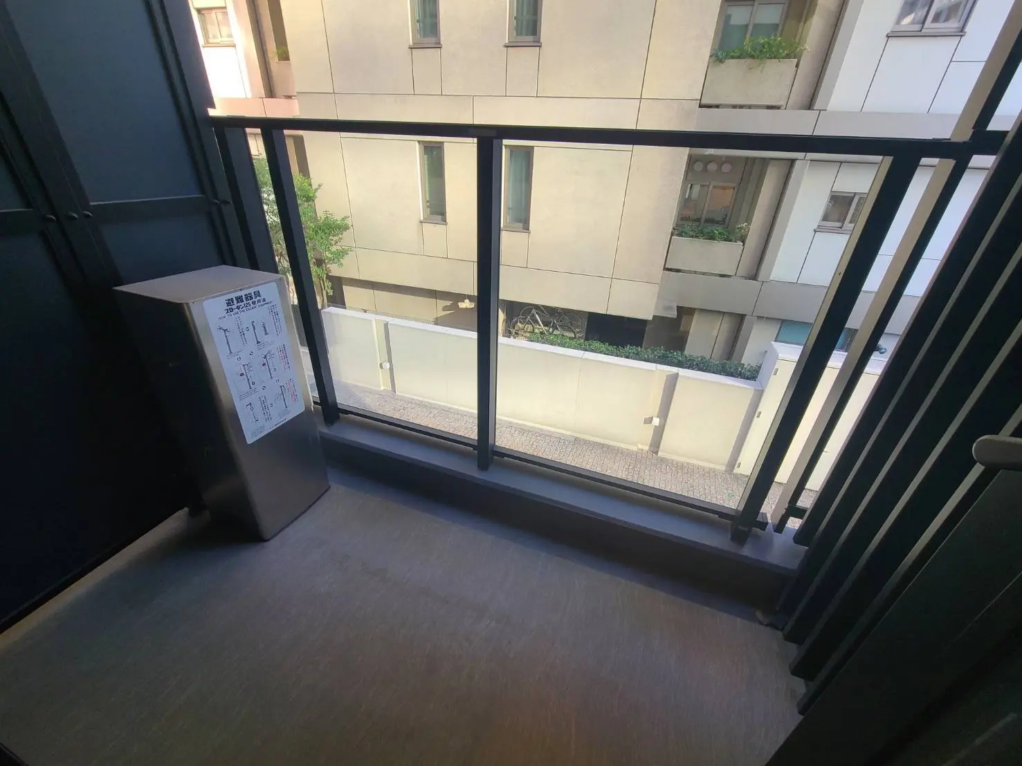 モダンなマンションのバルコニー、室外機が置かれた床、手すりと隣の建物の外観