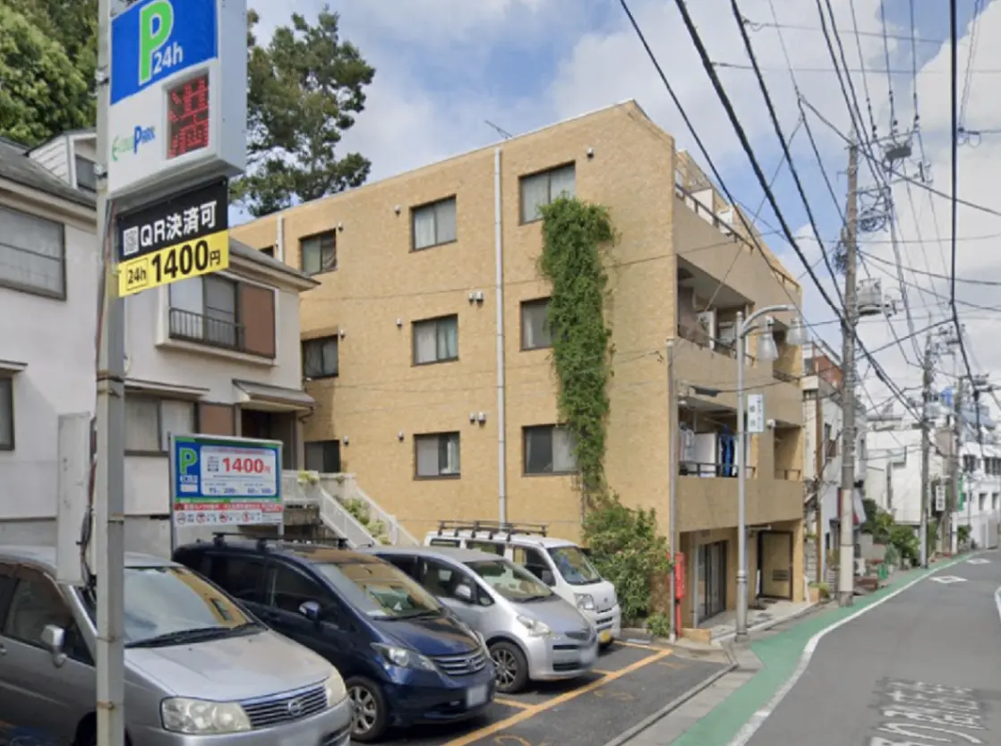 - 駐車場の看板が見える住宅街の風景、近くにアパートと駐車中の車両、電柱と電線が張り巡らされた通りの一コマ