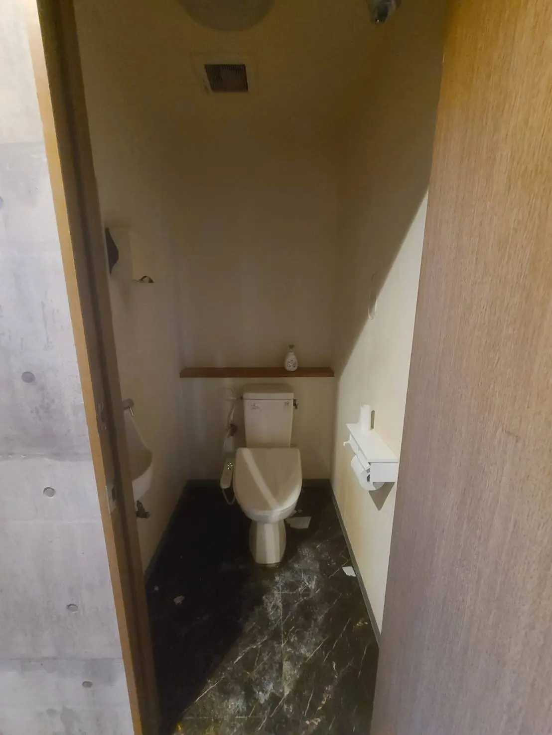 狭いトイレの内装、黒い大理石の床、壁掛けの小型の洗面台と紙巻器
