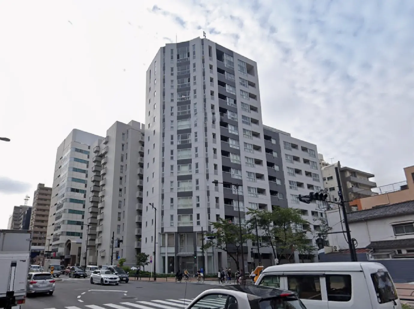 - 現代的なデザインの高層マンション、白と黒の外観、周囲に並ぶ他の建物と交通の様子を捉えた街の風景