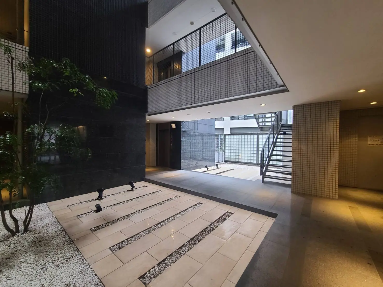 モダンなレジデンスのエントランスホール、白と黒のタイル、緑の植物、自然光が差し込む明るい空間