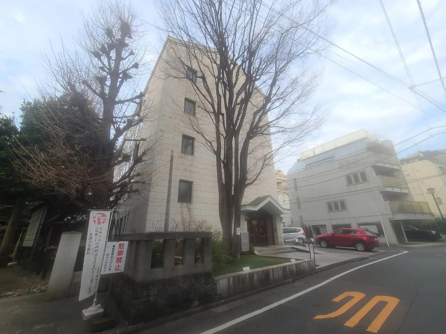 都市の風景、背の高い木々がそびえるビル、日本の住宅街、道路標識と電線が見える